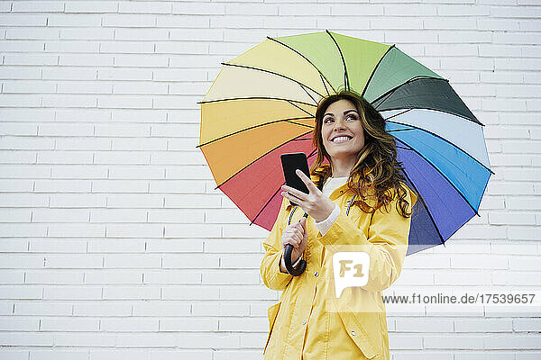 Woman holding smart phone and umbrella in front of brick wall