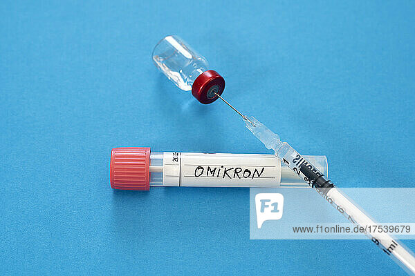 Medical syringe in vial with Omicron swab tube against blue background