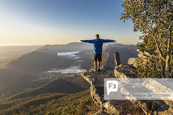 Australia  Victoria  Halls Gap  Male tourist standing with outstretched arms at edge of Boroka Lookout at dawn