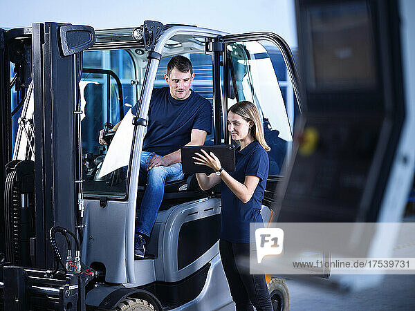 Engineer sharing digital tablet with coworker in forklift