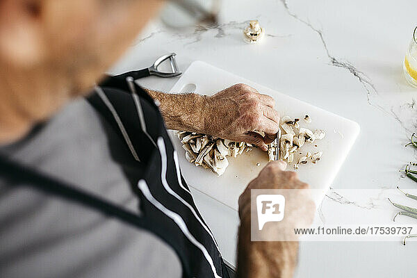 Man cutting mushrooms on cutting board at kitchen counter