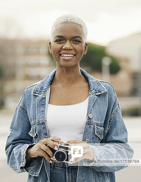 Smiling woman in denim jacket holding old camera