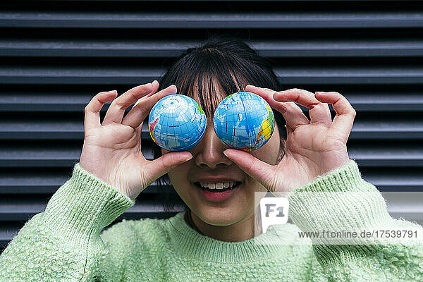 Playful woman covering eyes with toy globes