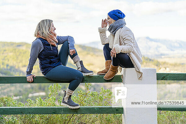 Female friends talking with each other sitting on railing