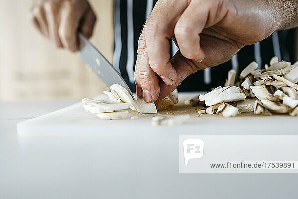 Mann schneidet zu Hause Pilze mit Küchenmesser auf Schneidebrett