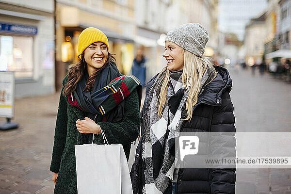 Woman with shopping bag looking at friend walking on footpath