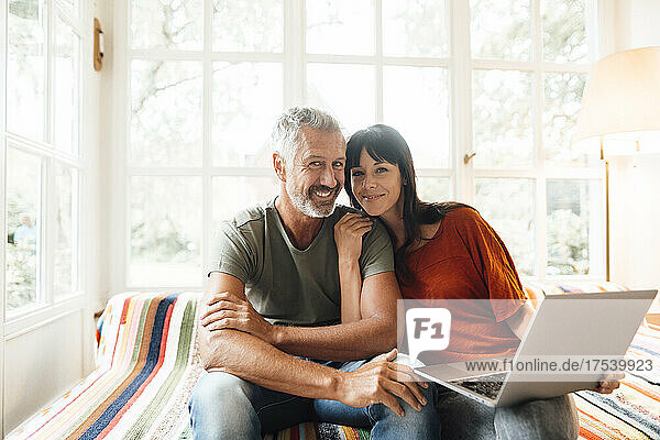 Happy couple with laptop sitting at home
