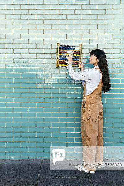 Young woman holding abacus on turquoise brick wall