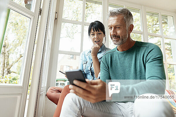 Man using smart phone sitting by surprised woman at home