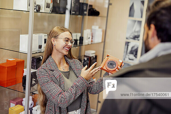 Glückliche Frau zeigt einem Freund im Geschäft eine Sofortbildkamera