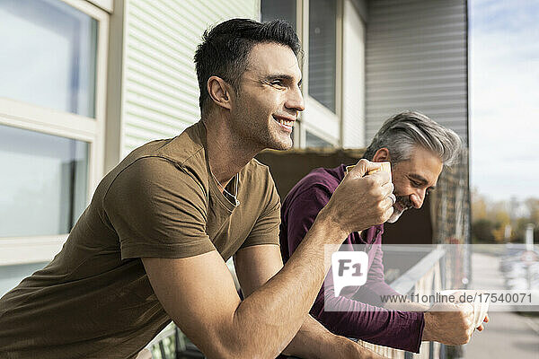 Smiling gay couple enjoying coffee together at balcony
