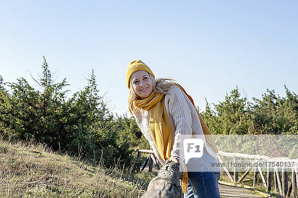 Woman in knit hat and scarf leaning on wooden bridge