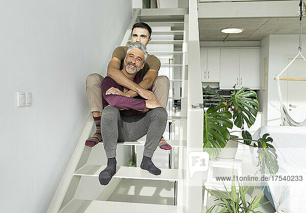 Smiling gay couple embracing on steps at home