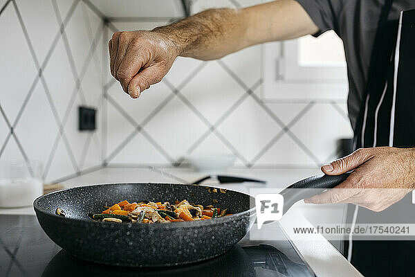 Man sprinkling salt on vegetables in frying pan