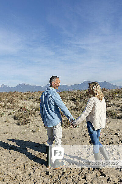 Man and woman holding hands standing at dunes
