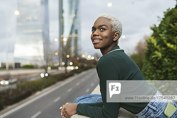Smiling woman leaning on wall in city at dusk