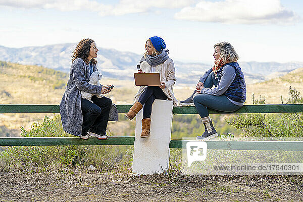 Woman holding laptop discussing with friends sitting on railing