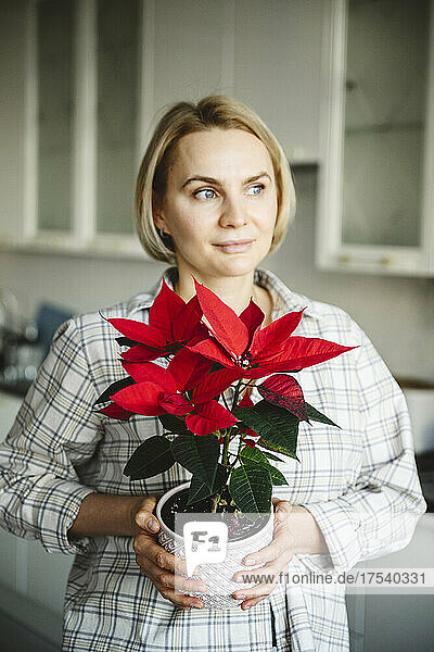 Nachdenkliche Frau hält Weihnachtssternpflanze zu Hause