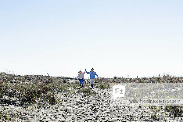 Glückliches Paar läuft auf Sand und genießt gemeinsam ein sonniges Wochenende