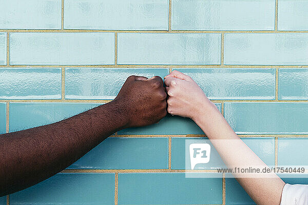 Multiracial friends giving fist bump on turquoise brick wall
