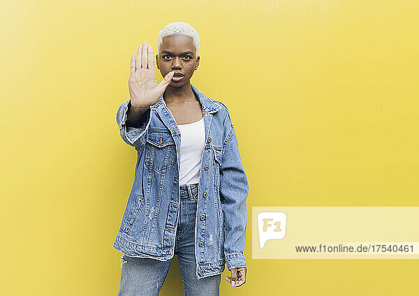 Serious woman making stop gesture standing against yellow background