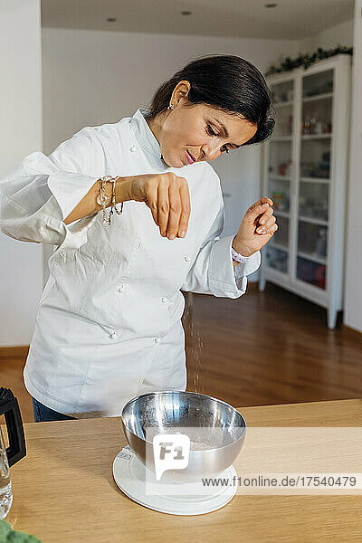 Chef adding pinch of salt in steel bowl on table at home