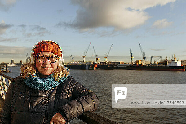 Smiling senior woman with headphones at harbor
