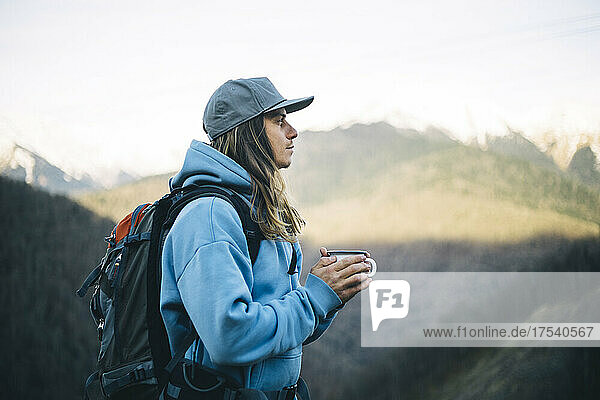 Contemplative man with coffee mug carrying backpack on vacation