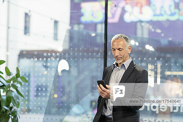 Businessman using smart phone in front of glass wall
