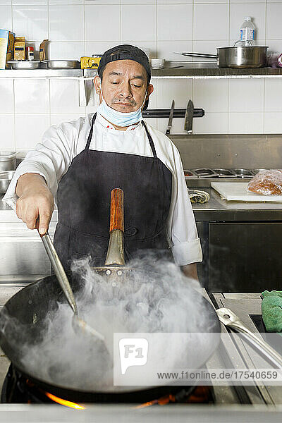 Chef cooking in wok on stove at restaurant kitchen