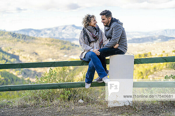 Romantisches Paar schaut einander auf dem Geländer sitzend an