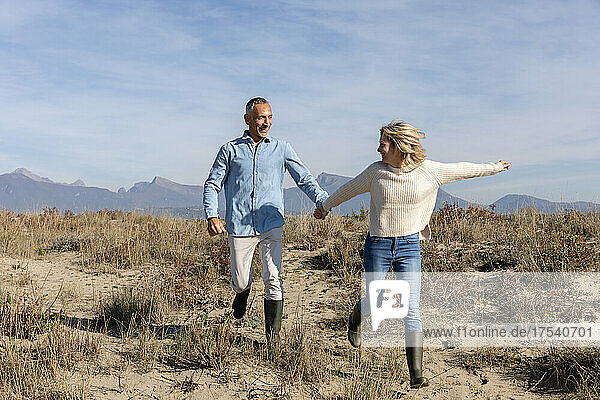 Fröhliches Paar hält Händchen beim Laufen in den Dünen