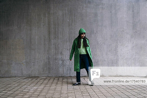 Young woman in green winter coat standing on footpath