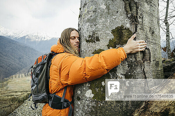 Tourist in orange jacket embracing tree trunk
