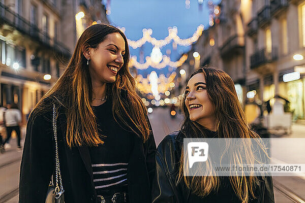 Young friends smiling at each other walking in city