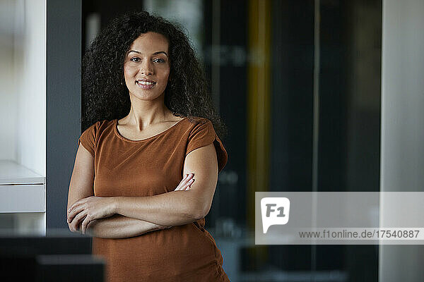 Smiling businesswoman leaning with arms crossed at workplace