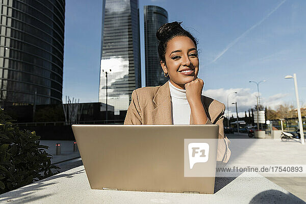 Smiling freelancer with laptop sitting at table on sunny day