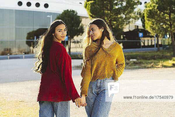 Young sisters holding hands standing on street in city together