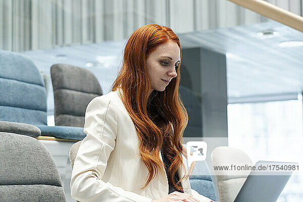 Working redhead woman using laptop sitting in auditorium at office