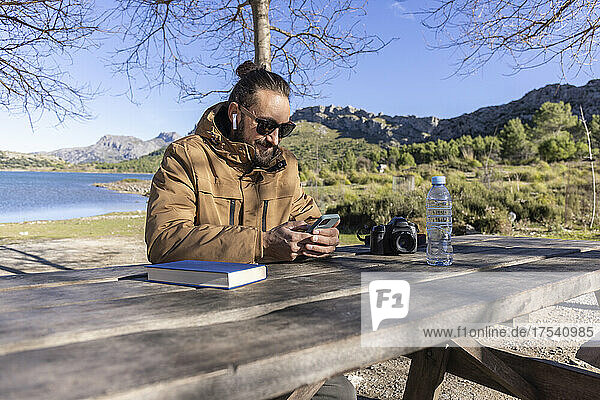 Man using smart phone and listening music through in-ear headphones at table  Cuber Dam  Mallorca  Balearic Islands  Spain
