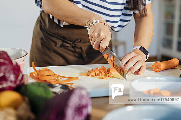 Woman cutting carrot on cutting board at home