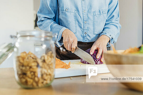 Woman cutting red cabbage on cutting board at home
