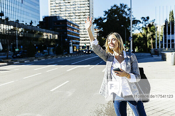 Young businesswoman hailing ride in city on sunny day