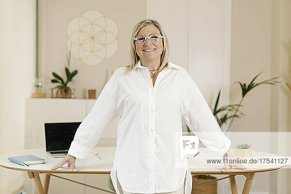 Smiling businesswoman standing in front of desk at workplace