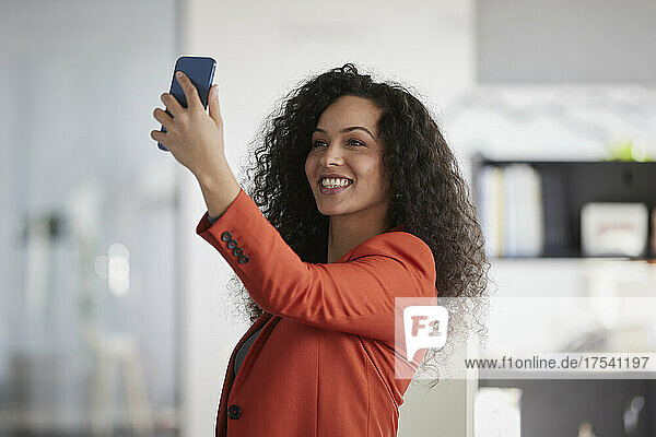 Smiling businesswoman taking selfie through smart phone at workplace
