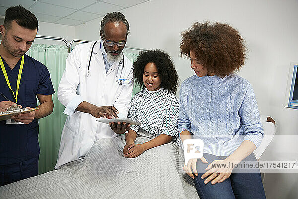 Patientin und Mutter überprüfen Bericht über Tablet-PC  der vom Arzt im Krankenhaus gehalten wird