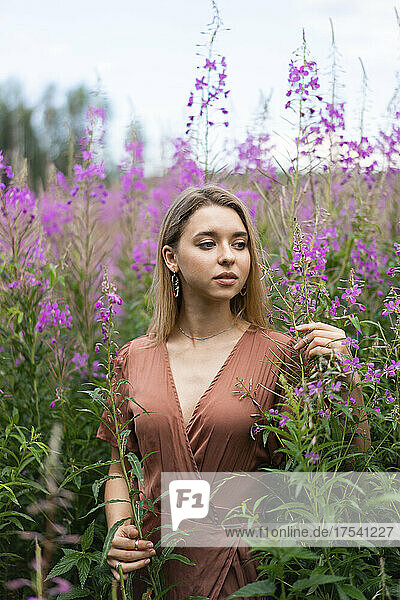 Thoughtful woman amidst flowering plants in meadow