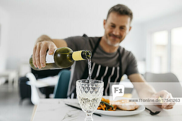Man pouring white wine in glass at home