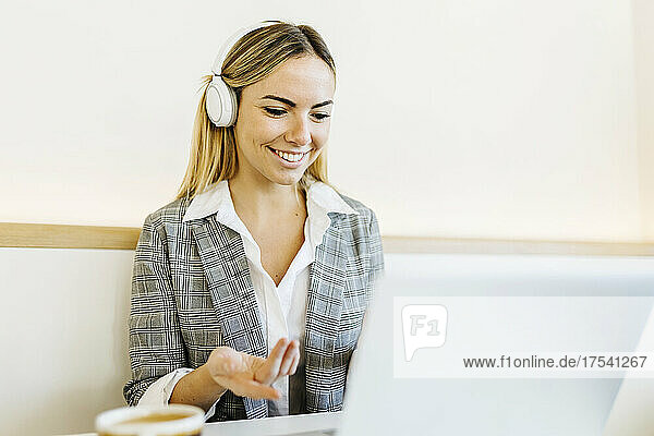 Smiling blond freelancer wearing headphones on video call through laptop in cafe