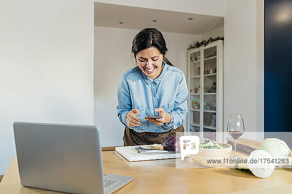 Smiling woman using smart phone standing at table